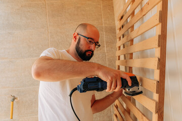 Man sanding wooden slats with power tool