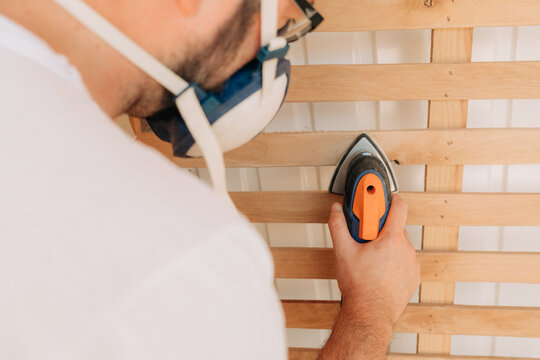 Close-up of a man sanding wood while wearing a mask
