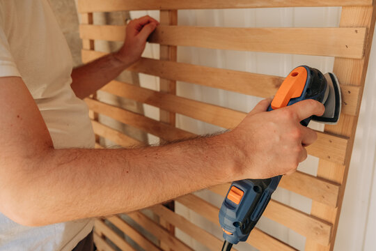 Close-up of man's hands using electric sander on wooden slats
