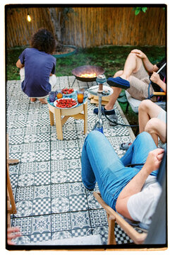 Group of anonymous men having fun, smoking hookah at the backyard 