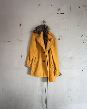 A yellow pea coat with a drawstring hanging on a concrete wall