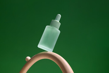 A green serum bottle is creatively balanced on a wooden ring