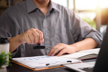 Hand using rubber stamp on business report at office desk. Ideal for legal process, authorization,...
