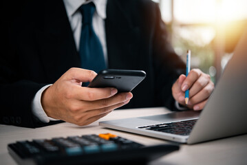 Business person interacting with mobile phone and laptop. Suitable for digital transformation, mobile banking, fintech, online work, and business planning visuals.