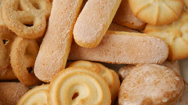 Vintage ceramic plate displaying colorful, golden-brown danish butter cookies and delicate ladyfingers, arranged in an appetizing, textural pattern against pristine white surface.