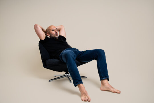 reclining on a black swivel chair with hands behind head