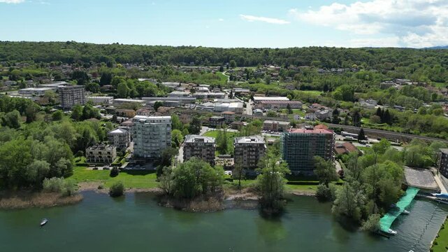 An expansive aerial view of a picturesque cityscape nestled alongside a tranquil lake, with modern architecture, lush greenery, and a sense of peaceful co-existence. Aerial view Lake Maggiore, Arona, 