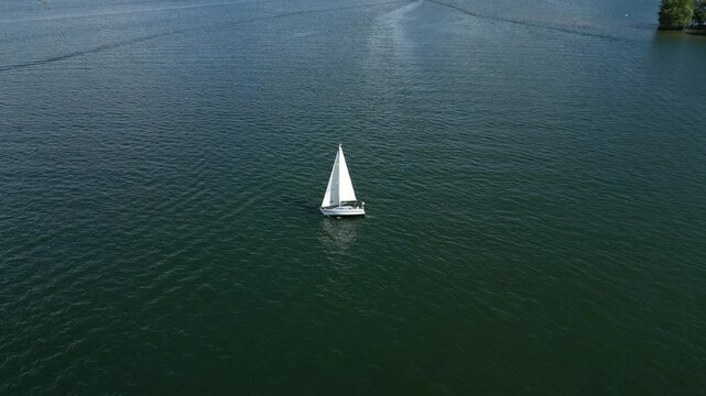 A lone sailboat glides across tranquil waters, its crisp white sail billowing gently as it navigates the open sea. Lake Maggiore, Arona, Italy