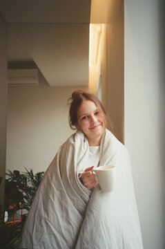 Teenager relaxing at home with a warm drink while wrapped in a blanket