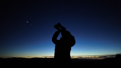 Amateur astronomer looking at the evening skies, observing planets, stars, Moon and other celestial objects with binoculars.
