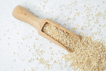 Scoop filled with sesame seeds on a light surface with scattered seeds