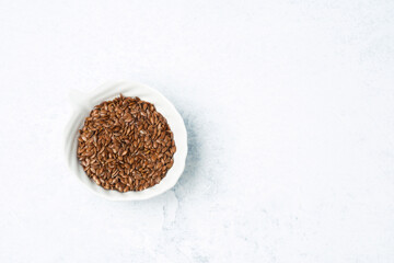 Brown flax seeds in a small white bowl on a textured background