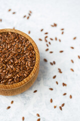 Flaxseeds in a wooden bowl with scattered seeds on a light surface