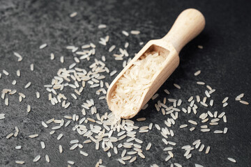 Rice grains scattered on a dark surface with a wooden scoop nearby