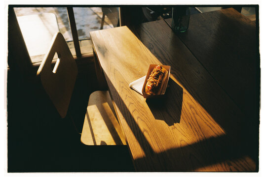 Hot dog resting on a wooden table in a sunlit cafe 