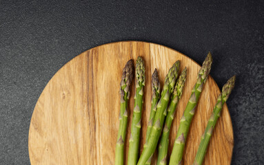 Fresh green asparagus spears await preparation on a round wooden board