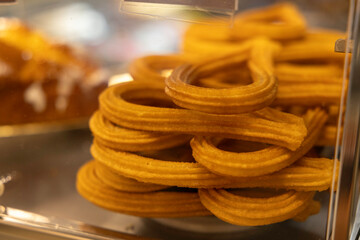 Golden-brown churros are stacked in a display case