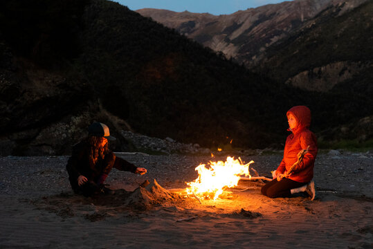 Siblings camping enjoying a fire at night, South Island, New Zealand.
