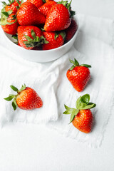 Fresh strawberries in a white bowl on a napkin against a light background