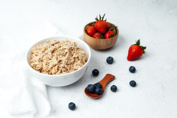 Oatmeal served in a bowl alongside fresh strawberries and blueberries
