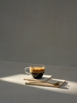 A clear glass cup of rich espresso rests on stone coasters
