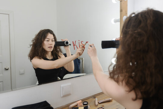 Vlogger filming makeup tutorial and writing kiss on mirror
