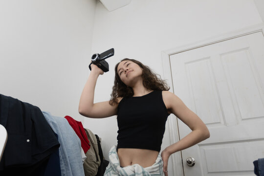 Young woman filming with a camcorder in her bedroom