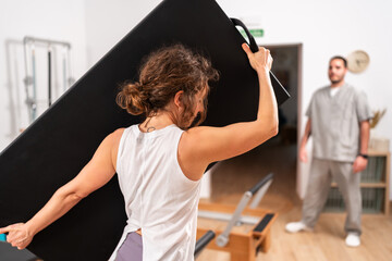 Woman carrying pilates reformer box in studio with instructor watching