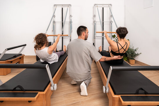 Instructor assisting women exercising on pilates reformer machine