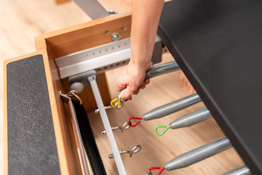 Woman adjusting springs on pilates reformer machine for exercise