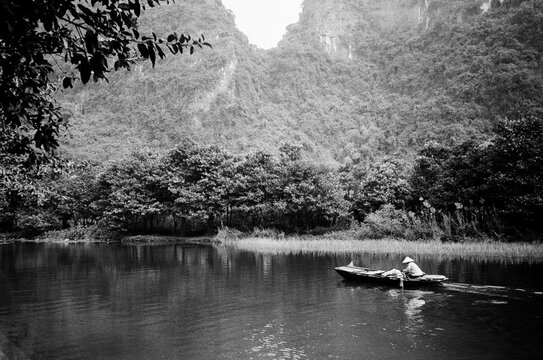 Film scan of a Vietnamese person with a hat rowing on canoe.