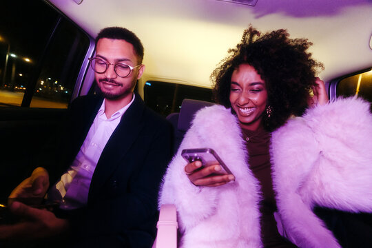 Two friends using phones inside a car at night 