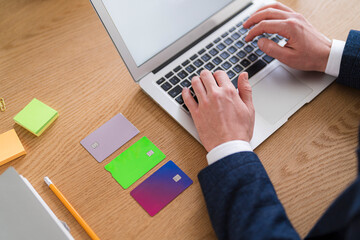 A man types on a laptop with multiple credit cards on the desk. He is managing his finances and banking online.
