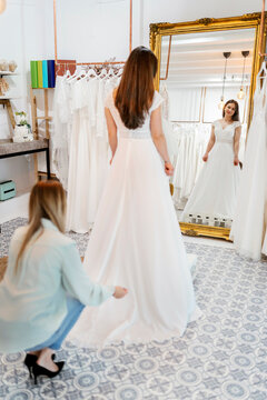 Wedding planner adjusting bride's dress in bridal boutique