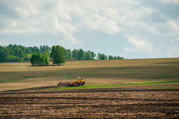 Obraz premium A yellow tractor works in a field on a farm in the spring 