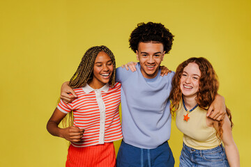Three happy students embracing and smiling on yellow background