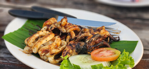 Fresh Grilled caramari squid with sweet sauce serving on banana leave on timber table