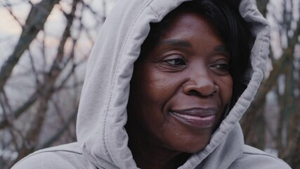 A elderly mature woman breathes fresh air and enjoys the snowfall in the winter forest. Winter walks and activity concept. Senior woman wearing winter wear in snow landscape - Powered by Adobe