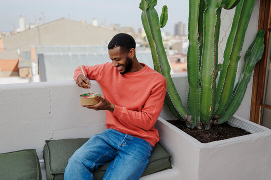 Happy man eating food on rooftop terrace with city view