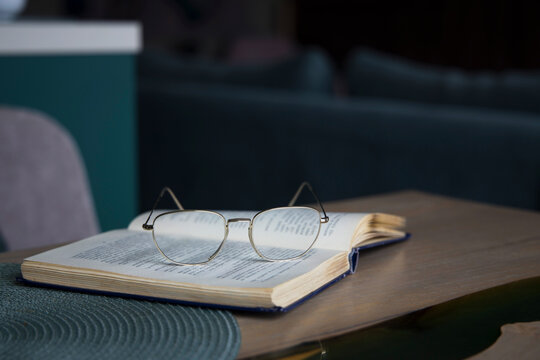 Open book resting on wooden table with glasses - Powered by Adobe