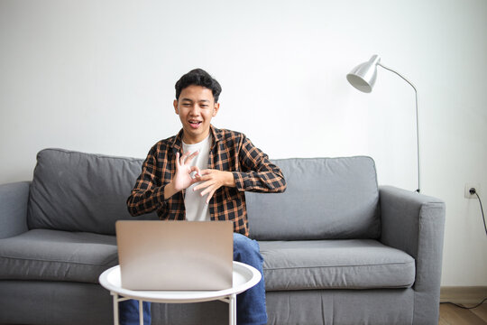 Hearing impaired boy in casual wear using sign language to his friend on video call online by laptop at home