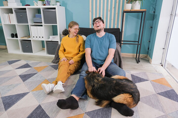 happy couple sitting on sofa near dog in living room