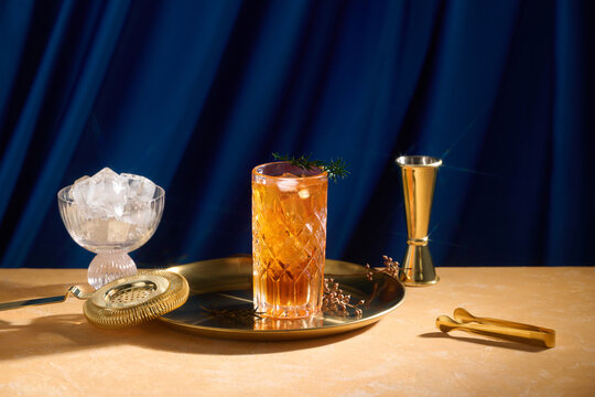 Amber cocktail in a crystal glass on gold tray with bar tools.