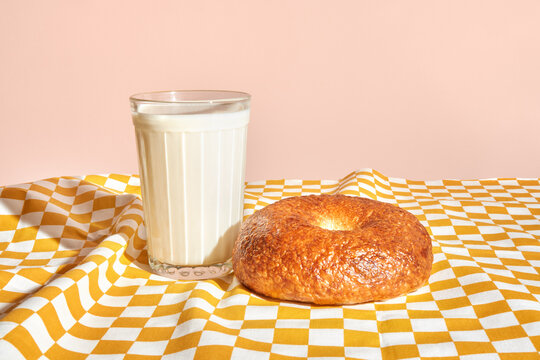 Freshly baked bagel with a glass of milk on a checkered tablecloth. 