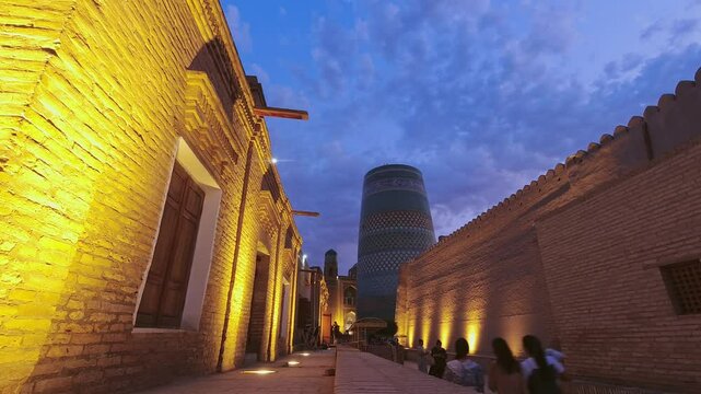 Khiva, Uzbekistan - 10th september, 2023: Night time lapse Ichan-Kala. Beautiful lighting of ancient buildings, Kalta Minar and madrasah. Khiva, UZBEKISTAN. Tourists walk through the city at night