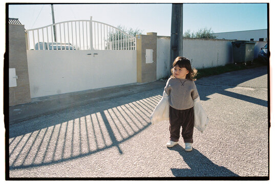 Toddler standing in sunlight casting long shadows on quiet stree