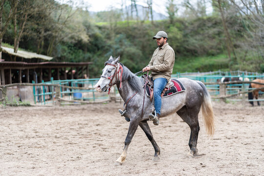 Young latin man riding grey horse inside riding school
