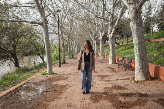 Woman walking along a tree-lined riverside path in the city