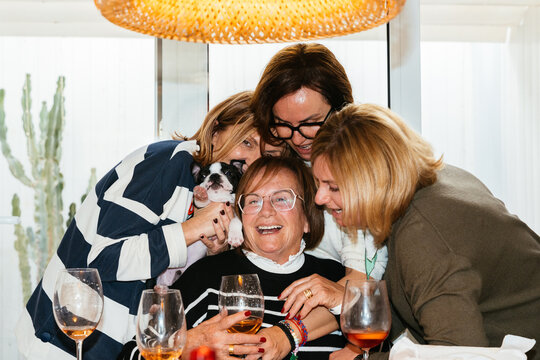 Four cheerful women hugging a senior woman and a puppy at home