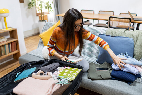 Woman checking her holidays travel list while packing suitcase